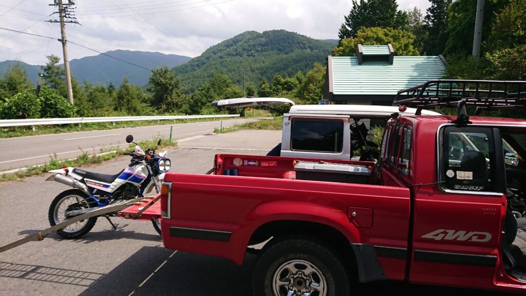 せん。 一人の整備士として、またバイク乗りとして泥臭いことをやってきた自分が、失敗を繰り返しながら「あ、これが一番心地いいな」って思えるものを見つけた独り言です。 「へぇ~」くらいで、気楽に読み流してくれれば嬉しいです。 誰かの正解じゃなく、読んでくれたの旅を見つけるための何かしらの「ヒント」になれば。そんな願いを込めて、書き進めてみます。 旅行じゃない旅!! 不自由な自由を求める。 旅って言うと大げさな感じですが、旅行ってなんだか決められた行程をこなす作業のように感じてちょっと疲れてしまうんです。 もちろん、ツーリングや複数人で行くときはそれはそれで楽しいんですけどね。 やっぱり思った通り自由に行動できるっていいなって思うんです。 「感じのよい川見つけた!!釣りしたい!!」 「今日はここで寝ようかな…」 「あっちの細い山道の先、何があるんだろう…」 「ここで飯を食う!」 そんな風に、その時の気分だけでハンドルを切る。 この先の天候が悪ければ行き先を変える。 渋滞してたら脇道を進む。 全部を自分で決めて、全部自分に返ってくる。この「不自由を楽しむ余裕」こそ、最高の遊びだと思うんです。 着続けた革ジャンを自分で塗り直したり、動かなくなったバイクをちまちま直したりするのも同じで、誰かに用意されたピカピカの新品じゃなく、自分の手で「走れる状態」にした相棒と、あえて不便な、行かないような場所へ行く。 直感でハンドルを切って、行き止まりだったら「あちゃー」って笑って引き返す。 そんな、端から見れば「無駄」だと思える時間の中にこそ、自分だけの本当の自由が詰まっている気がするんです。 車は拠点 バイクは翼 「バイクで行けばいいじゃん」ってよく言われるんですけど、車載旅には、それとはまた別の「極上の自由」があるんです。 自分にとってプロシード(ピックアップ)は、どこでも眠れる「家」であり、大切な道具を詰め込んだ「移動ガレージ」的なツールでもあるんです。 高速道路の退屈な移動や、突然の雨は車の中でやり過ごす。 で、ここぞという最高のワインディングや、細い路地の匂いを感じたい場所に着いたら、そこで初めて「翼」を降ろすんです。 重い荷物を車に預けて、身軽になったバイクで地元の空気を切り裂く。この瞬間の軽快さは、一度味わっちゃうともう戻れません。 自分の手で仕上げた相棒を、自分の運転するトラックで運ぶ。 バックミラー越しに、がっちり固定されたバイクの姿を確認するたび、「さあ、どこまで行こうか」ってニヤけちゃう。 車という「拠点」があるからこそ、バイクという「翼」でどこまでも遠くへ、安心して飛び立てる。このセットが、僕の最強のツールなんです。 自由の代償 自由って最高ですけど、そこには必ず「自分の身は自分で守る」っていう代償がついて回ります。それを痛烈に感じたのが、海外でバイクを借りたときでした。 プーケットの路地裏で借りた、見た目だけは派手なスクーター。いざ走り出してブレーキを握ったら、指がレバーを通り越してグリップに付きそうなくらいスカスカだったんです。「あ、これ死ぬかもな」って、一瞬で背中が凍りつきました。 タイヤをよく見れば、カチカチに硬化してヒビだらけ。もしあのままスコールの路面に突っ込んでいたら、今頃こうしてブログなんて書いていられなかったはずです。 「借り物だから動けばいい」なんて甘い考えは、異国の地では通用しません。 自由を最後まで楽しみ切るためには、相応の「備え」が必要なんです。 だからこそ僕は、どんな旅先でも自分の眼を信じるし、日本で自分の相棒に向き合うときは、ネジ一本の締め付けにもこだわるようになりました。 「最悪」を想定して、最高に楽しむ。 それが、不器用な僕なりにたどり着いた旅の作法なんです。 旅をとめない!! 僕が現場で最低限、これだけは譲れないのは「三種の神器」のチェック。 タイヤの「鮮度」:溝があるからOK、じゃないんです。ゴムが硬くなってないか、ひび割れてないか。 チェーンの「張り」:ダルダルだったり錆びてたりするのは、ただのパワーロス。最悪、旅先で外れたらそこで試合終了です。 ブレーキの「確信」:握った時に「止まる!」と確信できるか。レバーの遊びやパッドの残量、ここをケチるくらいなら旅には出ない方がいい。 「知識」っていうと難しく聞こえますが、これは相棒に対する「礼儀」みたいなもんです。 自分の手で少しずつ整えて、100%信頼できる状態で走り出す。この準備の時間があるからこそ、道の上で何が起きても「まあ、なんとかなる」と笑っていられる。 目的地は着いたところ 「どこまで行くの?」って聞かれるのが一番困ります(笑)。 僕にとっての目的地は、あらかじめ地図にピンを打った場所じゃない。走って、走って、「あ、ここいいな」ってエンジンを切った、その場所が目的地なんです。 広島の静かな夜の空気とか、プーケットの鼻につく熱い風、台湾の雑多な路地の匂い。 そんな、観光ポスターには載らないような「なんてことない景色」が、僕の旅の宝物です。自分で直し、自分で運び、自分の足でたどり着いたからこそ、そこは僕だけの特別な「聖地」になる。 「予定通りにいかないこと」を楽しむのが旅。 道に迷って、予定外の場所で真っ暗になっても、そこにプロシードがあればそこが寝床。 目的地に縛られず、今この瞬間、自分が立っている場所を面白がる。そんな不器用で自由な旅を、僕はこれからも続けていきたいと思っています。 旅は自立 人生、思うようにいかないことばかりですよね。 仕事で理不尽な思いをしたり、人間関係に疲れたり。僕だって、ただただ「やってらんねぇな」って投げ出したくなる夜は何度もありました。 でも、この不自由な旅を繰り返す中で、一つだけ学んだことがあります。 それは、**「自分で自分の機嫌を取り、自分の足で立つ」**という方法です。 壊れたら自分の手で直せばいい。道が塞がっていたら、別のルートを探せばいい。 そうやって旅先で一つひとつ問題をクリアしていくたび、少しずつ自分がタフになっていくのを感じるんです。この「自律」の感覚こそが、日常に戻ったときの自分を支える、目に見えない最強の武器になります。 完璧な準備なんていらなくて、まずは隣町まで走ってみる。 ボロい革ジャンを塗り直した時のような、あの小さな一歩の積み重ねが、いつの間にかあんたを遠い場所まで連れて行ってくれるはずです。 ここまで読んでくれて、ありがとう。 次はどこかの道の上で会いましょう。あんたの旅も、心から応援しています。