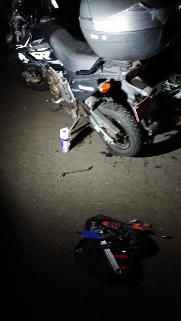 せん。 一人の整備士として、またバイク乗りとして泥臭いことをやってきた自分が、失敗を繰り返しながら「あ、これが一番心地いいな」って思えるものを見つけた独り言です。
「へぇ~」くらいで、気楽に読み流してくれれば嬉しいです。
誰かの正解じゃなく、読んでくれたの旅を見つけるための何かしらの「ヒント」になれば。そんな願いを込めて、書き進めてみます。
旅行じゃない旅!!
不自由な自由を求める。
旅って言うと大げさな感じですが、旅行ってなんだか決められた行程をこなす作業のように感じてちょっと疲れてしまうんです。
もちろん、ツーリングや複数人で行くときはそれはそれで楽しいんですけどね。
やっぱり思った通り自由に行動できるっていいなって思うんです。
「感じのよい川見つけた!!釣りしたい!!」
「今日はここで寝ようかな…」
「あっちの細い山道の先、何があるんだろう…」
「ここで飯を食う!」
そんな風に、その時の気分だけでハンドルを切る。
この先の天候が悪ければ行き先を変える。
渋滞してたら脇道を進む。
全部を自分で決めて、全部自分に返ってくる。この「不自由を楽しむ余裕」こそ、最高の遊びだと思うんです。
着続けた革ジャンを自分で塗り直したり、動かなくなったバイクをちまちま直したりするのも同じで、誰かに用意されたピカピカの新品じゃなく、自分の手で「走れる状態」にした相棒と、あえて不便な、行かないような場所へ行く。
直感でハンドルを切って、行き止まりだったら「あちゃー」って笑って引き返す。
そんな、端から見れば「無駄」だと思える時間の中にこそ、自分だけの本当の自由が詰まっている気がするんです。
車は拠点 バイクは翼
「バイクで行けばいいじゃん」ってよく言われるんですけど、車載旅には、それとはまた別の「極上の自由」があるんです。
自分にとってプロシード(ピックアップ)は、どこでも眠れる「家」であり、大切な道具を詰め込んだ「移動ガレージ」的なツールでもあるんです。
高速道路の退屈な移動や、突然の雨は車の中でやり過ごす。
で、ここぞという最高のワインディングや、細い路地の匂いを感じたい場所に着いたら、そこで初めて「翼」を降ろすんです。
重い荷物を車に預けて、身軽になったバイクで地元の空気を切り裂く。この瞬間の軽快さは、一度味わっちゃうともう戻れません。
自分の手で仕上げた相棒を、自分の運転するトラックで運ぶ。 バックミラー越しに、がっちり固定されたバイクの姿を確認するたび、「さあ、どこまで行こうか」ってニヤけちゃう。
車という「拠点」があるからこそ、バイクという「翼」でどこまでも遠くへ、安心して飛び立てる。このセットが、僕の最強のツールなんです。
自由の代償
自由って最高ですけど、そこには必ず「自分の身は自分で守る」っていう代償がついて回ります。それを痛烈に感じたのが、海外でバイクを借りたときでした。
プーケットの路地裏で借りた、見た目だけは派手なスクーター。いざ走り出してブレーキを握ったら、指がレバーを通り越してグリップに付きそうなくらいスカスカだったんです。「あ、これ死ぬかもな」って、一瞬で背中が凍りつきました。
タイヤをよく見れば、カチカチに硬化してヒビだらけ。もしあのままスコールの路面に突っ込んでいたら、今頃こうしてブログなんて書いていられなかったはずです。
「借り物だから動けばいい」なんて甘い考えは、異国の地では通用しません。 自由を最後まで楽しみ切るためには、相応の「備え」が必要なんです。 だからこそ僕は、どんな旅先でも自分の眼を信じるし、日本で自分の相棒に向き合うときは、ネジ一本の締め付けにもこだわるようになりました。
「最悪」を想定して、最高に楽しむ。 それが、不器用な僕なりにたどり着いた旅の作法なんです。
旅をとめない!!
僕が現場で最低限、これだけは譲れないのは「三種の神器」のチェック。
タイヤの「鮮度」:溝があるからOK、じゃないんです。ゴムが硬くなってないか、ひび割れてないか。
チェーンの「張り」:ダルダルだったり錆びてたりするのは、ただのパワーロス。最悪、旅先で外れたらそこで試合終了です。
ブレーキの「確信」:握った時に「止まる!」と確信できるか。レバーの遊びやパッドの残量、ここをケチるくらいなら旅には出ない方がいい。
「知識」っていうと難しく聞こえますが、これは相棒に対する「礼儀」みたいなもんです。 自分の手で少しずつ整えて、100%信頼できる状態で走り出す。この準備の時間があるからこそ、道の上で何が起きても「まあ、なんとかなる」と笑っていられる。
目的地は着いたところ
「どこまで行くの?」って聞かれるのが一番困ります(笑)。 僕にとっての目的地は、あらかじめ地図にピンを打った場所じゃない。走って、走って、「あ、ここいいな」ってエンジンを切った、その場所が目的地なんです。
広島の静かな夜の空気とか、プーケットの鼻につく熱い風、台湾の雑多な路地の匂い。 そんな、観光ポスターには載らないような「なんてことない景色」が、僕の旅の宝物です。自分で直し、自分で運び、自分の足でたどり着いたからこそ、そこは僕だけの特別な「聖地」になる。
「予定通りにいかないこと」を楽しむのが旅。 道に迷って、予定外の場所で真っ暗になっても、そこにプロシードがあればそこが寝床。 目的地に縛られず、今この瞬間、自分が立っている場所を面白がる。そんな不器用で自由な旅を、僕はこれからも続けていきたいと思っています。
旅は自立
人生、思うようにいかないことばかりですよね。 仕事で理不尽な思いをしたり、人間関係に疲れたり。僕だって、ただただ「やってらんねぇな」って投げ出したくなる夜は何度もありました。
でも、この不自由な旅を繰り返す中で、一つだけ学んだことがあります。 それは、**「自分で自分の機嫌を取り、自分の足で立つ」**という方法です。
壊れたら自分の手で直せばいい。道が塞がっていたら、別のルートを探せばいい。 そうやって旅先で一つひとつ問題をクリアしていくたび、少しずつ自分がタフになっていくのを感じるんです。この「自律」の感覚こそが、日常に戻ったときの自分を支える、目に見えない最強の武器になります。
完璧な準備なんていらなくて、まずは隣町まで走ってみる。 ボロい革ジャンを塗り直した時のような、あの小さな一歩の積み重ねが、いつの間にかあんたを遠い場所まで連れて行ってくれるはずです。
ここまで読んでくれて、ありがとう。 次はどこかの道の上で会いましょう。あんたの旅も、心から応援しています。